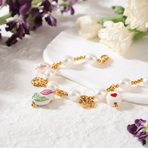 Detail of pearl bracelet featuring floral ceramic beads and golden charms on white background