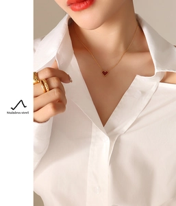 Close-up of a red heart pendant necklace on a gold chain worn with a white shirt