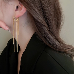 Close-up of golden long tassel heart earrings worn by a model against black background