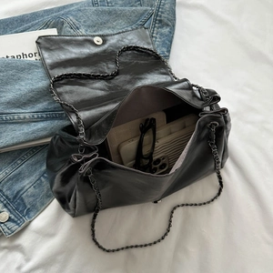 Vintage black chain tote bag with pleated texture on white bedding with accessories