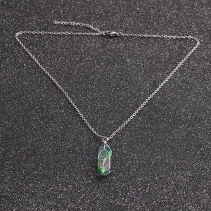 Macro detail of wire-wrapped green crystal pendant with silver chain on dark background