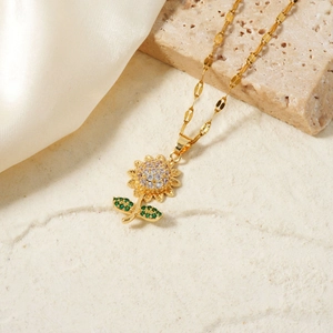 Golden sunflower necklace with sparkling cubic zirconia and green leaves on silk background