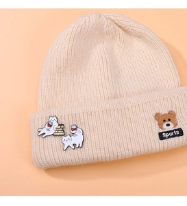 Detail of cute cat enamel pins on a beige knitted beanie with a brown bear patch