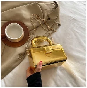 Detail of glossy gold acrylic clutch bag with rigid handle and fine metallic chain strap
