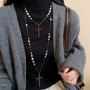 Detail einer mehrlagigen Perlenkette mit rotem Strasskreuz-Anhänger auf Pullover
