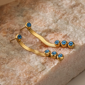 Bohemian gold snake chain drop earrings with blue evil eye beads on natural stone background