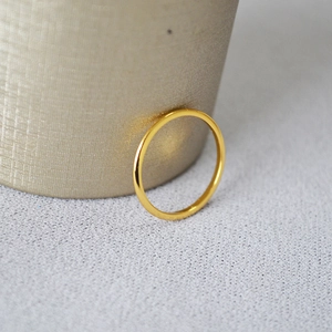 Close-up detail of a slim gold-plated wavy brass ring on a textured grey background