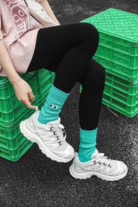 Detail of teal slouch socks with embroidered eye pattern worn with white sneakers