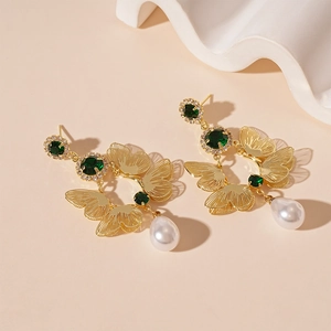 Macro shot of gold butterfly earrings with green stones and white teardrop pearls