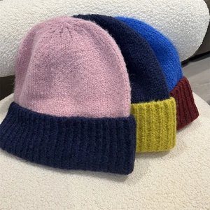 Close-up of three thick two-tone knit beanies in pink, navy, and blue on plush background