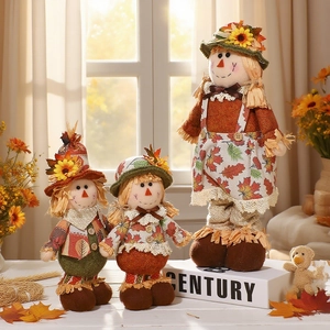Three autumn scarecrow plush dolls in various sizes on white wooden table with warm lighting