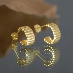 Detailed close-up of gold C-shaped ribbed stud earrings with premium metallic texture