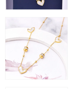 Detailed close-up of golden heart pendant necklace with white shells on marble surface