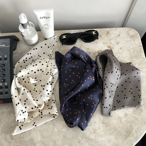 Flat lay of three silk scarves in beige, blue, and gray polka dot patterns on marble