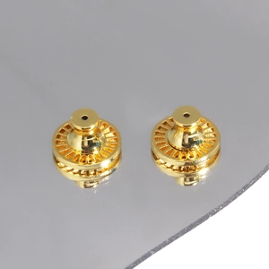 Detail of two gold metal earring lifters with textured edges on a gray surface