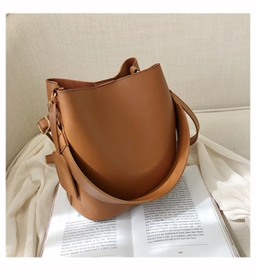 Detail view of a brown leather bucket bag with golden hardware on a soft beige background