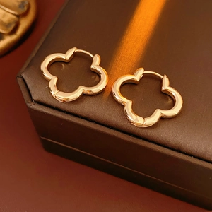 Macro shot of gold clover hoop earrings on a textured brown leather jewelry box