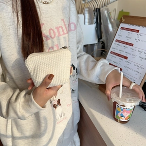 Détail de la texture gaufrée blanche d'une pochette cosmétique tenue dans un café