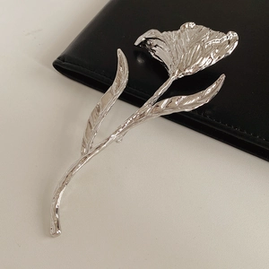 Close-up of a silver floral brooch with a polished mirror finish on black leather background