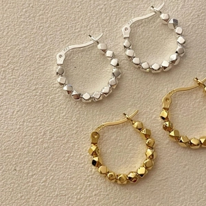 Detail of faceted bead hoop earrings in gold and silver 925 sterling silver on textured background