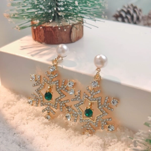 Detail of gold snowflake earrings with emerald stones and pearls on festive snow