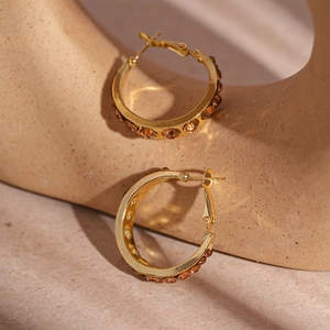 Golden geometric hoop earrings with amber crystals on a minimalist textured background