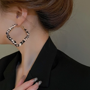 Close-up of zebra pattern leopard fabric wrapped large square hoop earrings on a model
