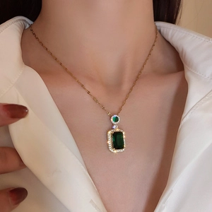 Macro view of gold chain necklace with rectangular emerald stone and diamond halo