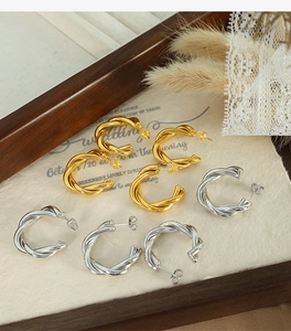 Close-up of twisted gold and silver C-shaped hoop earrings on a textured fabric
