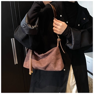 Close-up of brown suede shoulder bag with adjustable strap and decorative ribbon detail