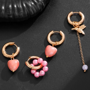 Detail of pink heart and hummingbird asymmetrical gold earrings set with pearls