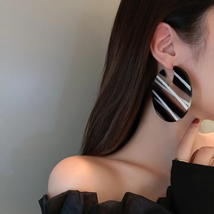 Close-up of oversized black and white striped acrylic C-shape hoop earring worn by a model