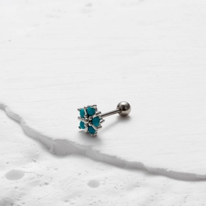 Macro detail of silver cartilage stud with turquoise flower design on stone surface