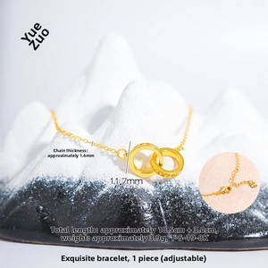 Macro detail of 24K gold interlocking double ring bracelet with heart charm and clasp