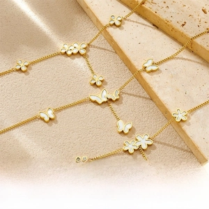Macro detail of gold-plated chain featuring butterfly and four-leaf flower charms with inlays