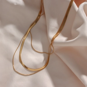 Detail showing the layered 18K gold-plated snake chain necklaces on white silk fabric