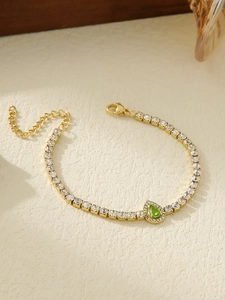 Detailed close-up of gold tennis chain bracelet with white zircons and green pear-cut stone