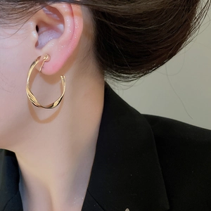 Macro side view of elegant golden twisted hoop earrings worn by a model on ear