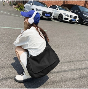 Side view of large black canvas messenger bag worn by a model in outdoor setting