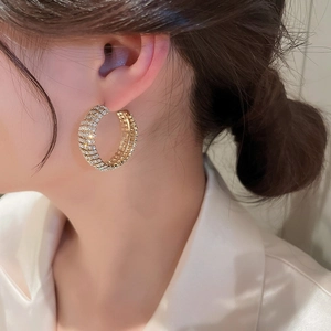Elegant gold-tone C-shaped hoop earrings with sparkling rhinestones worn by a model