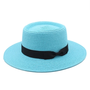 Detail of teal straw boater hat featuring fine weave texture and black ribbon bow accent