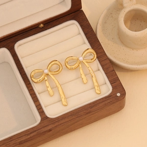 Close-up of golden bow earrings with center pearl in a premium wooden jewelry box