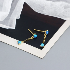 Macro detail of gold-plated long tassel earrings with blue synthetic opal in four-prong setting