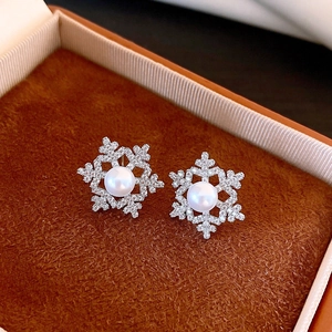 Detailed view of snowflake earrings with 18k gold plating, pearls and zircon on brown velvet