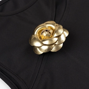 Detail of a golden 3D camellia floral brooch attached to a black knit fabric surface