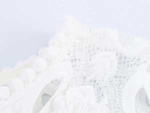 Gros plan sur un tissu en dentelle blanche avec broderies florales et petits détails de pompons