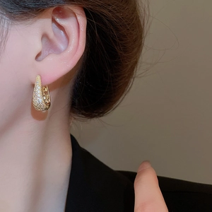 Gros plan de boucles d'oreilles dorées en U avec oxydes de zirconium blancs sur le lobe
