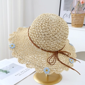 Detail of straw hat with blue floral embroidery and bow on a gold display stand