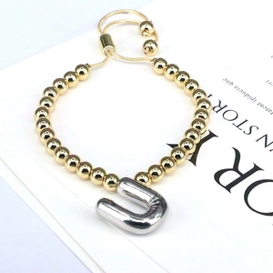 Detail of adjustable gold beaded bracelet with silver balloon-style letter U charm