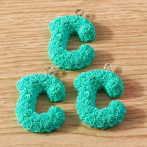 Three cyan resin C-shaped charms with 3D rose textures and metal rings on wood surface